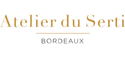 L'image est un logo avec le texte « Atelier du Sertissage » écrit en élégante police serif dorée sur la ligne supérieure. En dessous, une fine ligne horizontale dorée le sépare du mot « BORDEAUX » écrit en lettres majuscules noires. Le fond est blanc.