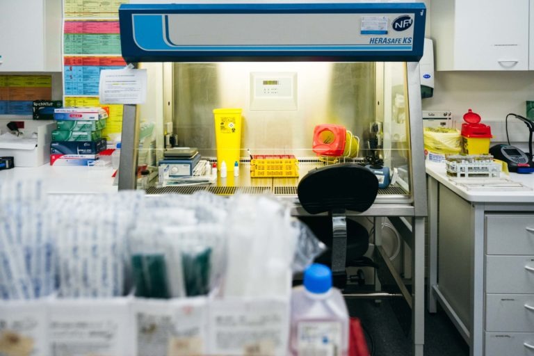 Un poste de travail de laboratoire équipé d'une enceinte de biosécurité HERAsafe KS, faisant partie de l'initiative Héros Méconnus du CH d'Angoulême. Le poste de travail contient diverses fournitures de laboratoire, notamment des tubes, un conteneur à déchets et des gants. Au premier plan, on peut voir en flou d'autres fournitures et équipements de laboratoire. L'environnement du laboratoire est organisé et stérile.