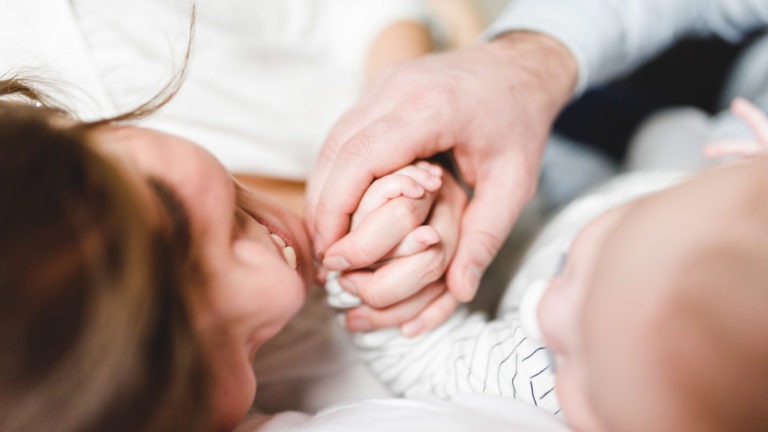 Un plan rapproché montre un adulte tenant doucement la main d'un bébé. La main de l'adulte berce les petits doigts du bébé, évoquant un sentiment de tendresse et de connexion. Ce moment intime reflète l'importance des souvenirs d'enfance, l'adulte et le bébé étant tous deux doucement flous en arrière-plan.