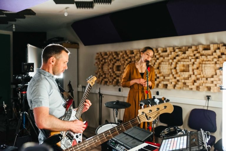 Le duo Altalina, talentueux duo girondin, se produit dans un studio d'enregistrement. Un homme joue de la guitare électrique tandis qu'une femme chante dans un micro. Le studio est doté de mousse insonorisante sur les murs et de divers instruments, dont une guitare basse, un clavier et une batterie. L'ambiance est concentrée et professionnelle.