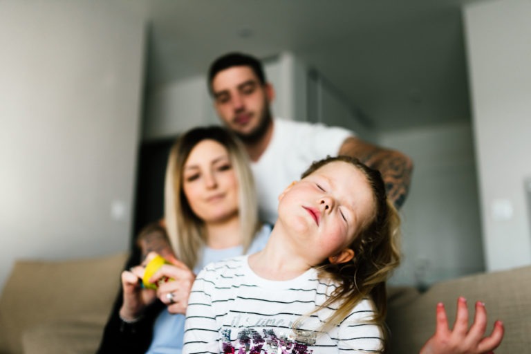 Une jeune fille aux cheveux châtain clair, vêtue d'une chemise rayée, est assise sur un canapé au premier plan, les yeux fermés et la tête penchée en arrière. Derrière elle, une femme aux longs cheveux blonds et un homme tatoué sur les bras, tous deux détendus, sont assis côte à côte, absorbés comme s'ils avaient subi un coup de foudre au feu rouge.