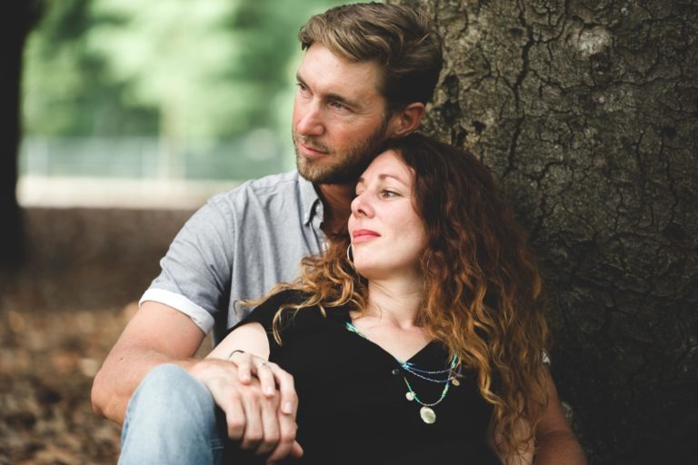 Un homme et une femme sont assis contre un arbre dans un parc. L'homme, aux cheveux courts et à la barbe, est assis derrière la femme, le regard perdu dans le vide. La femme, aux cheveux ondulés, pose sa tête sur son torse, l'air satisfait. Ils se sont rencontrés en tant qu'étrangers lors d'un coup de foudre au café Brun Bordeaux. Tous deux ont des expressions détendues ; l'arrière-plan est flouté par la verdure.