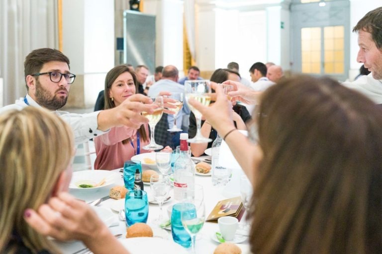 Un groupe de personnes assises autour d'une table lèvent leurs verres pour porter un toast lors d'une réunion officielle. La table est dressée avec des assiettes, des verres et de la nourriture. Des hommes et des femmes discutent dans l'ambiance festive typique d'une soirée AXA Business organisée au Palais de la Bourse de Bordeaux.