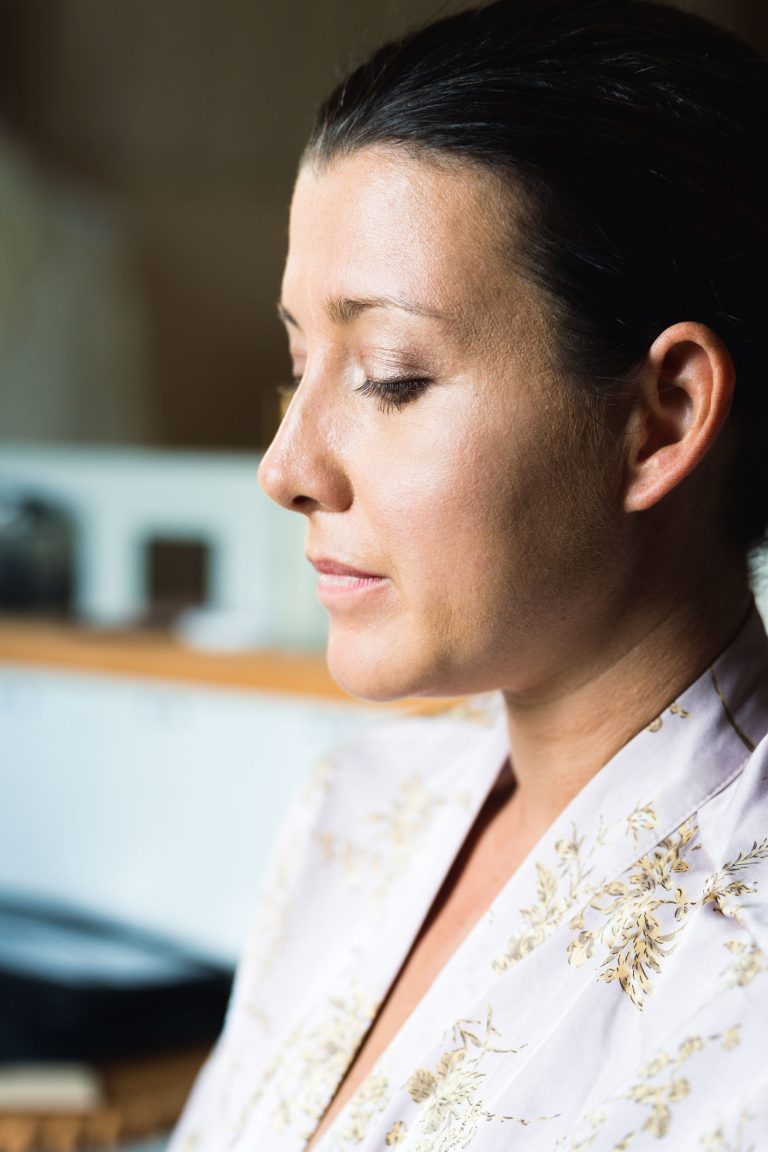 Une femme à la peau claire et aux cheveux foncés tirés en arrière est représentée de profil, vêtue d'une robe de chambre florale de couleur claire. Elle semble calme et détendue, baignée par une douce lumière naturelle - un moment de sérénité inspiré par la mariée de la Saint-Valentin.