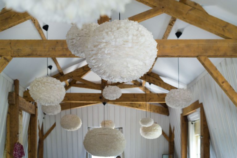 Dans une pièce aux poutres apparentes et aux murs lambrissés de blanc, de grandes suspensions duveteuses Antonin sont suspendues au plafond. L'atmosphère douce évoque le Château de Garde à Moulon, la lumière du soleil entrant par les fenêtres de droite.