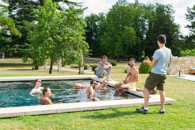 Sept jeunes adultes, dont Antonin et Valentine, se retrouvent autour d'une petite piscine rectangulaire en plein air. Six personnes sont assises ou debout dans ou près de la piscine, certaines portant des lunettes de soleil et des maillots de bain. Un homme se tient sur l'herbe avec une boisson à la main. Des arbres verdoyants occupent l'arrière-plan.