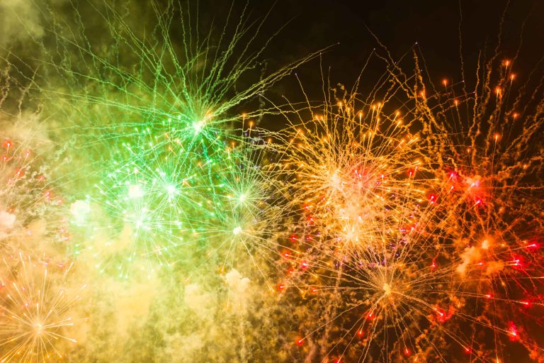Un feu d'artifice coloré explose dans le ciel nocturne au-dessus du Château de Garde à Moulon, avec des éclats lumineux de vert, de jaune et d'orange qui rayonnent vers l'extérieur. La fumée et les traînées scintillantes remplissent la scène festive, célébrant le marié Antonin sur la toile de fond sombre.
